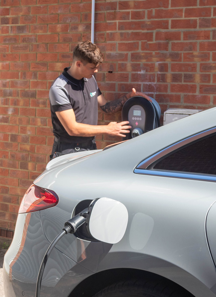 A car plugged into an EV charger with a Diamond Green Energy engineer at the unit